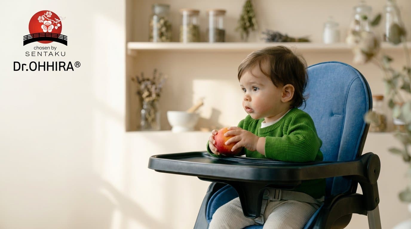 Väike laps rohelises kampsunis istub söögitoolis, hoides käes puuvilja. Taustal logo ja köögiriiulid.