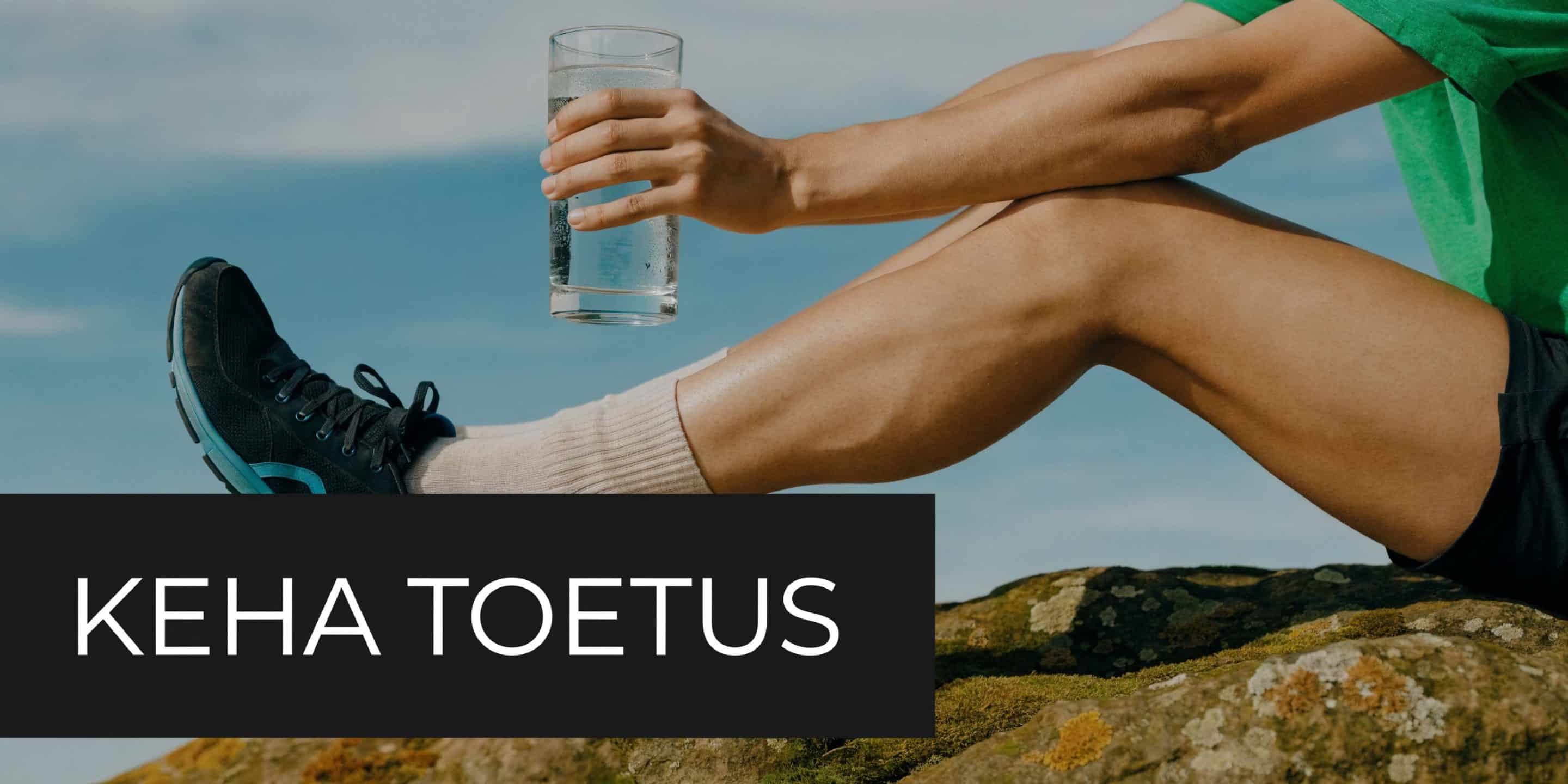 Sportlik inimene istub kivil, hoiab klaasi vett ja puhkab pärast füüsilist treeningut värskes õhus.