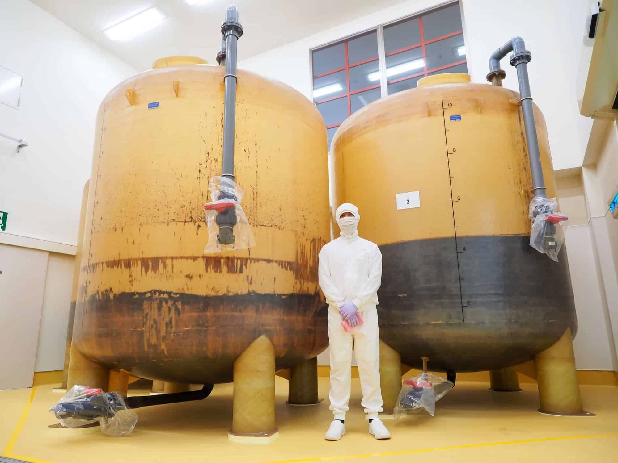 Isik valges kaitseülikonnas seisab kahe suure tööstusliku tsisterni vahel puhtas ruumis.